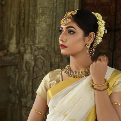 Beautiful Indian woman in traditional saree, adorned with exquisite jewelry, set against historic architecture.
